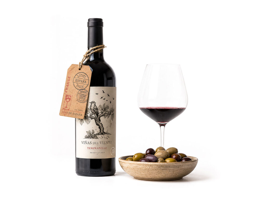 Botella de vino Tempranillo con etiqueta grabada y etiqueta kraft de exportación España, junto a copa de vino tinto y cuenco de aceitunas, ilustrando servicios de internacionalización para marcas agroalimentarias